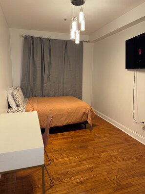 A bedroom with a bed, a desk, a chair, a television mounted on the wall, and a wooden floor. - 3 Bd 2 Ba Apt Chinatown (Philadelphia)