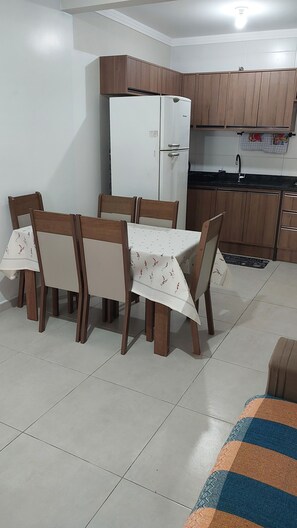 A compact kitchen with wooden cabinets, a white refrigerator, and a dining table with chairs. - New Listing (Florianópolis)