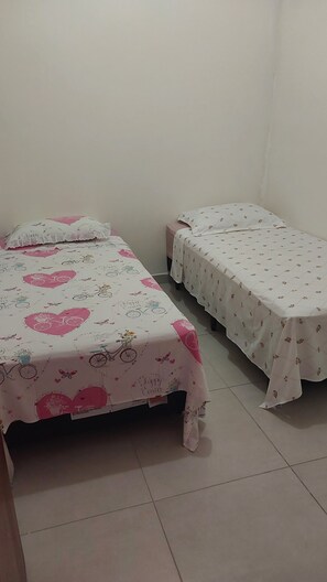 Two single beds with floral and bicycle-themed bedding, a plain wall, and a tiled floor. - New Listing (Florianópolis)