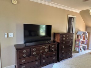 A room with a flat-screen TV, two dark wooden dressers with ornate handles, a white door, and a dollhouse. - Lake Murray Retreat , Fire Pit & Boat Ramp,1 Bedroom Loft (Chapin)