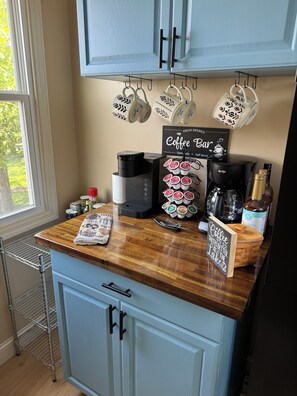 A kitchen counter with a coffee maker, coffee pods, a coffee bar sign, and a window with a view of greenery. - Lake Murray Retreat , Fire Pit & Boat Ramp,1 Bedroom Loft (Chapin)