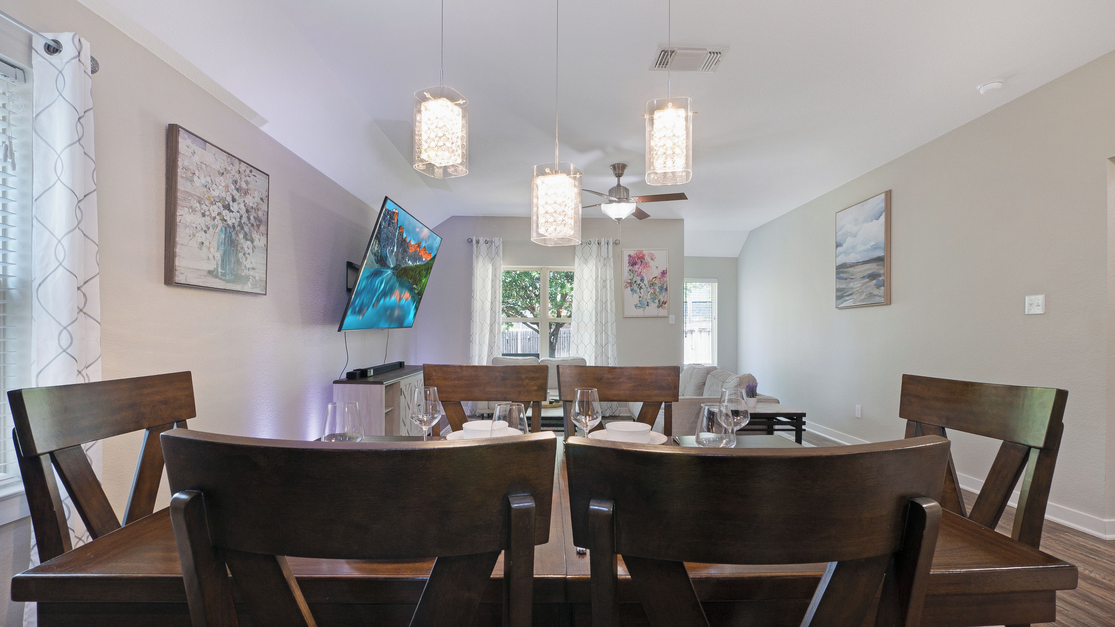 Zona pranzo con tavolo rotondo, sedie in legno, lampadari a sospensione e opere d'arte alle pareti.