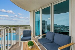 A balcony with a sofa, chairs, a small table, and a potted plant. - Escape to The Palms | Gulf Views, Resort Pool & Beach Gear (Destin)
