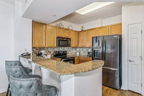 A kitchen with wooden cabinets, a granite countertop, a stainless steel refrigerator, and a built-in oven. - Escape to The Palms | Gulf Views, Resort Pool & Beach Gear (Destin)