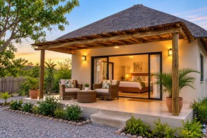 Un espacio de estar al aire libre cubierto con muebles de mimbre, una cama con vistas panorámicas y una estructura de techo de paja.