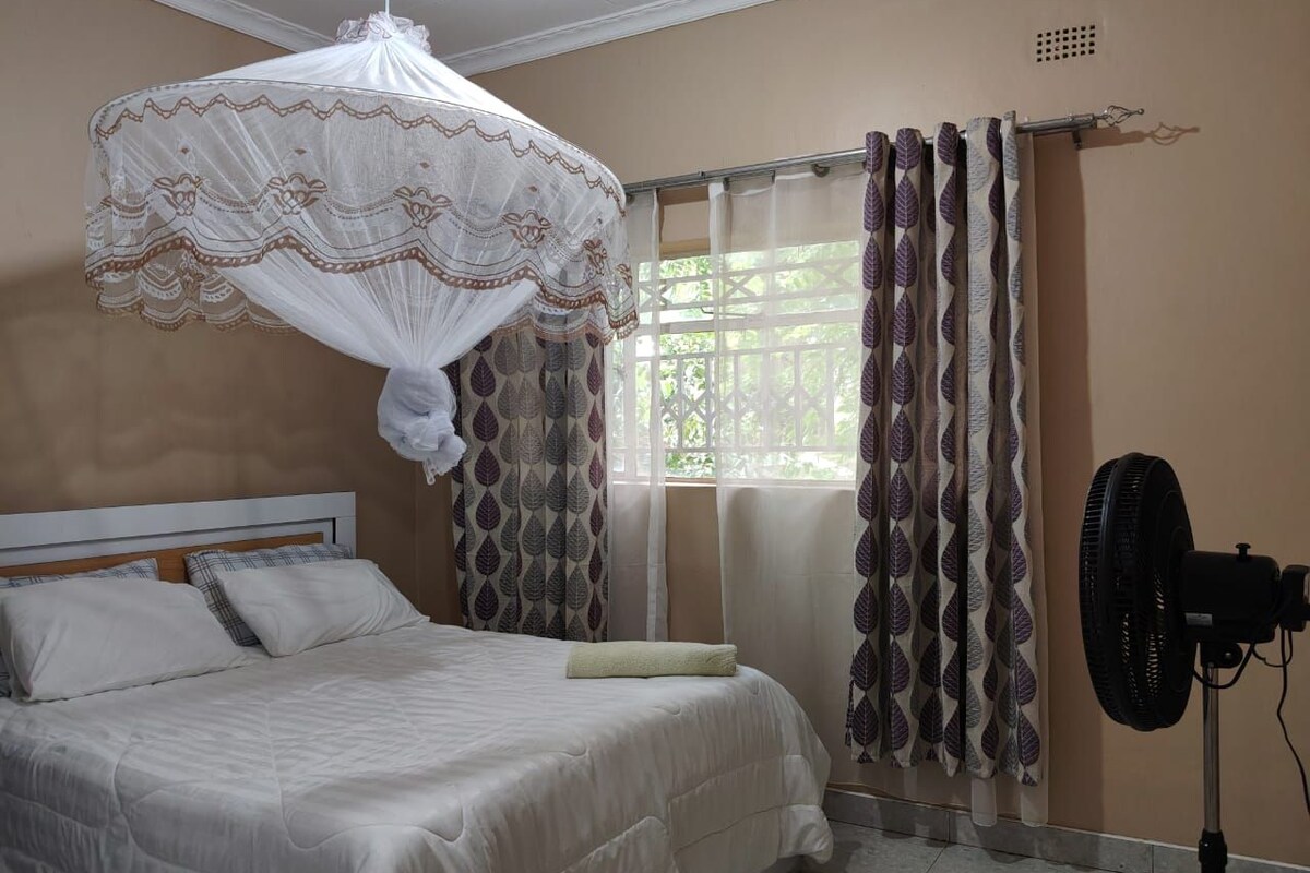 Un dormitorio con una cama, un ventilador en la mesita de noche y una ventana con cortinas.