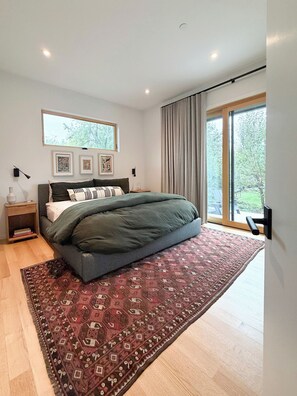 Een slaapkamer met een bed, nachtkastje, raam met gordijnen en uitzicht op de omgeving.