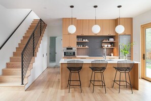 A modern kitchen with wooden cabinets, a central island with bar stools, and a staircase with black railings. - Modern guest house with incredible light, open floor plan, office and deck (Boulder)
