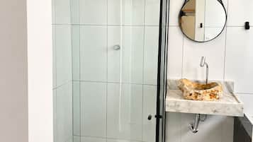 A modern bathroom with a glass-enclosed shower, a marble sink, and a round mirror.