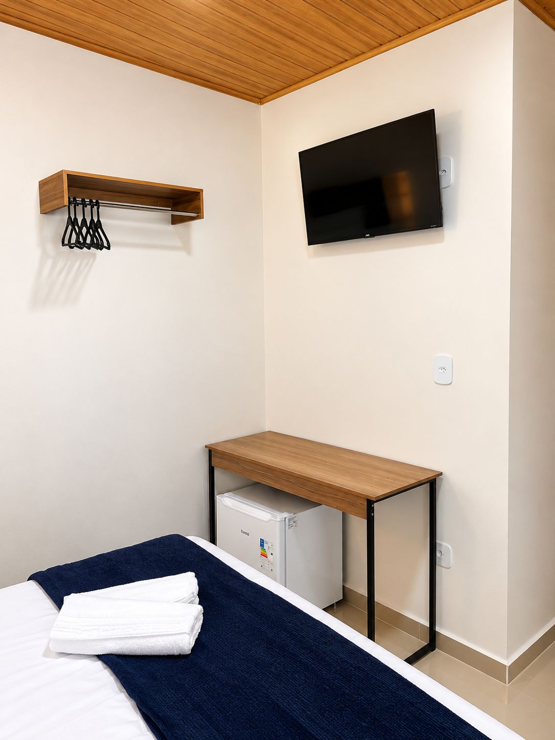 Ein Schlafzimmer mit einem Bett, einem Schreibtisch mit Computer, einem Fernseher und einem kleinen Kühlschrank.