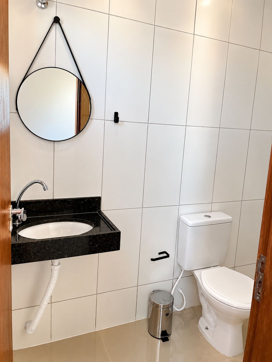 A bathroom with a white tiled wall, a black sink with a mirror, a toilet, and a trash can.