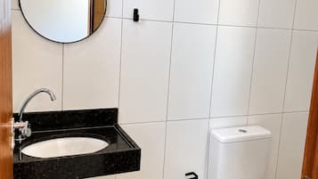 A bathroom with a white tiled wall, a black sink with a mirror, a toilet, and a trash can.