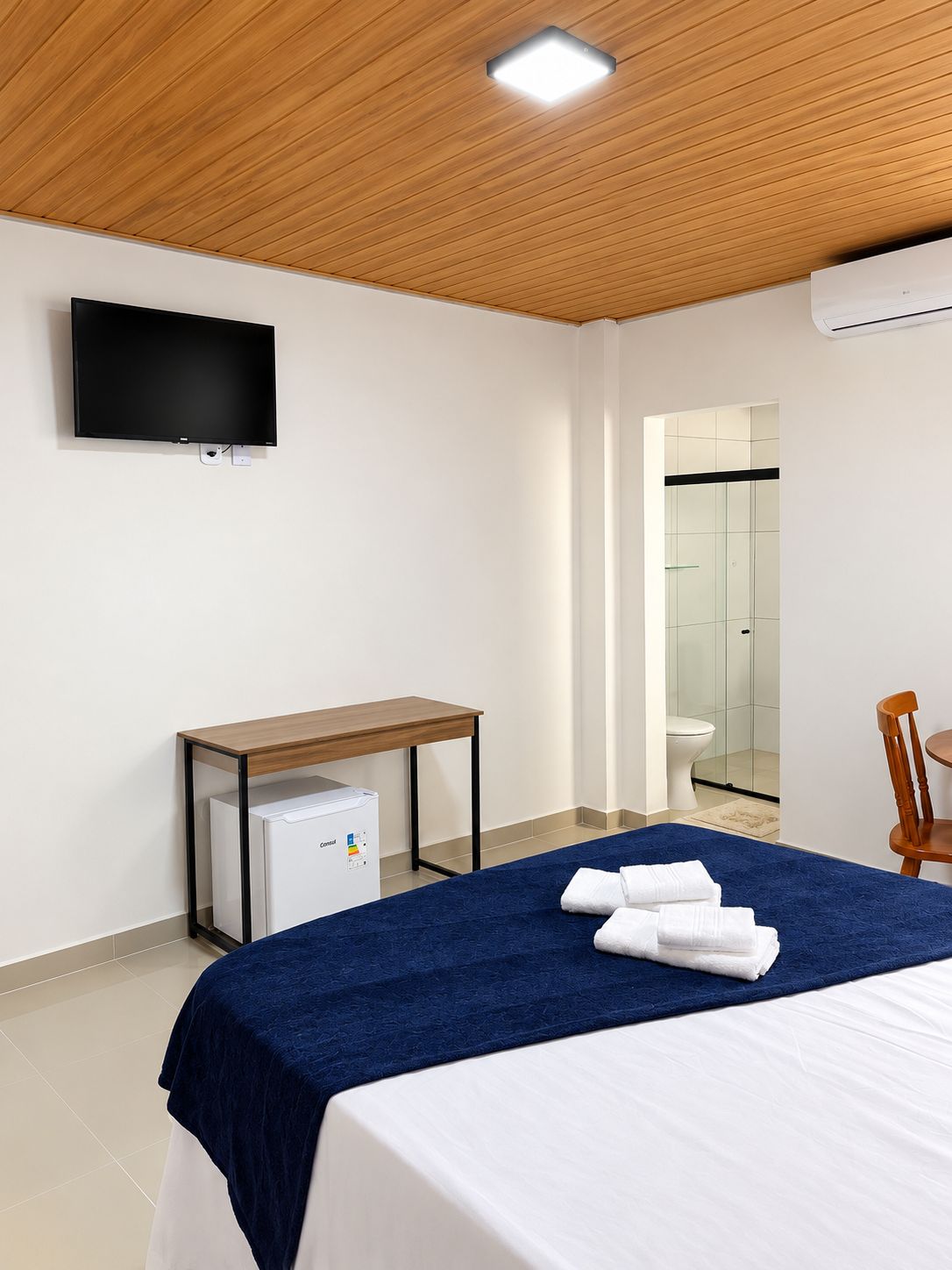 Una habitación de hotel con cama, escritorio, televisor y aire acondicionado.