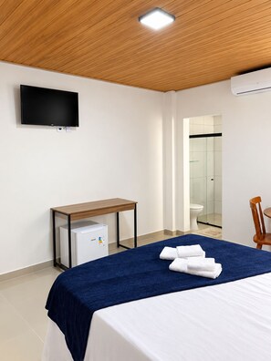Una habitación de hotel con cama, escritorio, televisor y aire acondicionado.