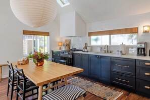 A modern kitchen with dark cabinets, a wooden dining table, and a skylight. - Two Stylish Cottages, One Coastal Escape | Walk to Beach | Dog Friendly (Cannon Beach)