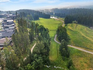 A golf course with a winding path, surrounded by dense forest and residential buildings. - Velaris | Downtown | Hot Tub | Mtn Views | Pets Ok (Canmore)