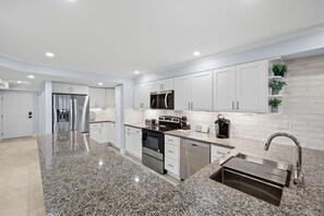 A modern kitchen with granite countertops, stainless steel appliances, and white cabinetry. - Pointe Santo E6- Beachfront Walkout Condo w/ Den (Sanibel)