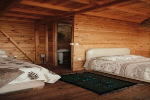 Un dormitorio tipo cabaña con dos camas, un baño pequeño y techo inclinado.