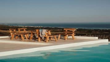 A pool with wooden benches and a view of the ocean.