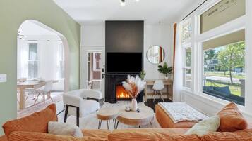 Een woonkamer met een open haard, een bank, een eethoek en uitzicht op de omgeving.