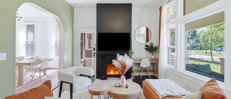 A living room with a fireplace, a sofa, a dining area, and a view of the outdoors.
