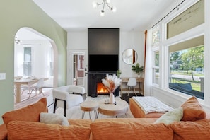Un salon avec une cheminée, un canapé, un coin repas et une vue sur l’extérieur.