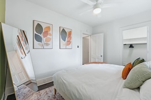 Une chambre à coucher avec un lit, un ventilateur de plafond, une porte et des œuvres d’art murales.