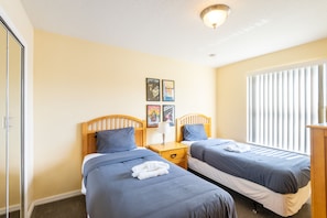 A hotel room with two single beds, a nightstand, a lamp, and a window with blinds. - 3BR Condo Near Disney w/ Pool, gym & Balcony (Kissimmee)