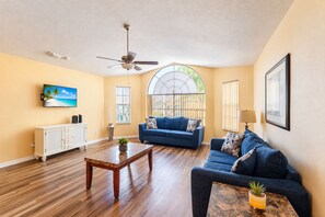 Sala de estar com ventilador de teto, uma janela ampla com vista, sofá azul e mesa de centro.