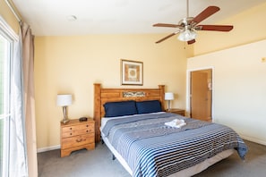 A bedroom with a bed, two bedside tables, a ceiling fan, a framed picture, and a door. - 3BR Condo Near Disney w/ Pool, gym & Balcony (Kissimmee)