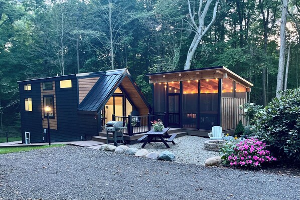 A modern cabin with a sloped roof, a deck, and a fire pit area.