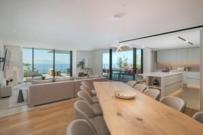 A modern living room with a large wooden dining table, beige sofas, and a view of the sea through large windows. - Savoy Luxe - Luxury 3-bed w/ pool (Funchal)