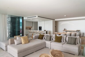A modern living room with a sectional sofa, a dining area with a wooden table, and a kitchen in the background. - Savoy Luxe - Luxury 3-bed w/ pool (Funchal)