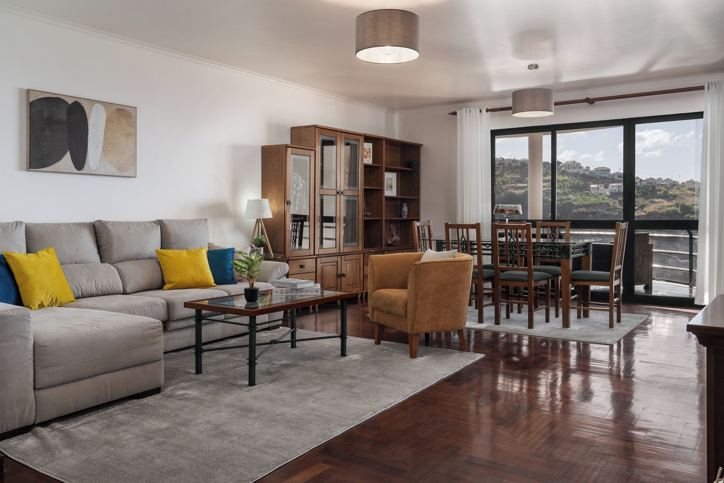 Un salon comprenant un canapé, une table basse et des fauteuils, une bibliothèque et une vue dégagée sur l’extérieur grâce à une grande fenêtre.