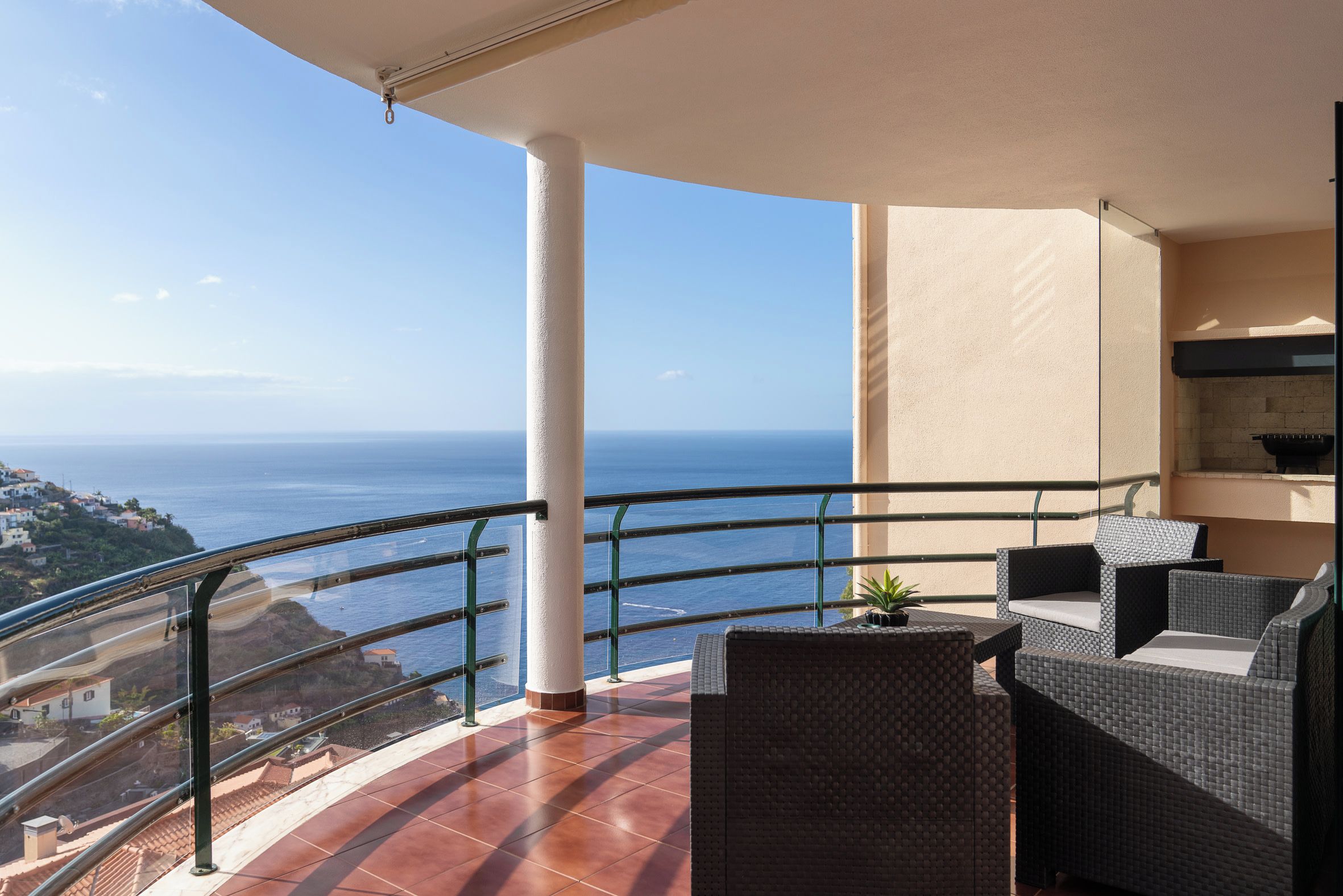 Un balcón con vista al mar, mobiliario exterior y suelo de baldosas.