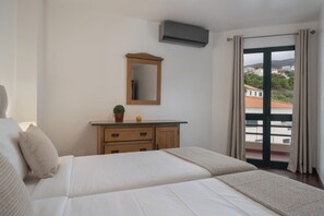 Ein Hotelzimmer mit einem Bett, einem Schminktisch, einem Spiegel und Blick auf Gebäude durch ein Fenster.