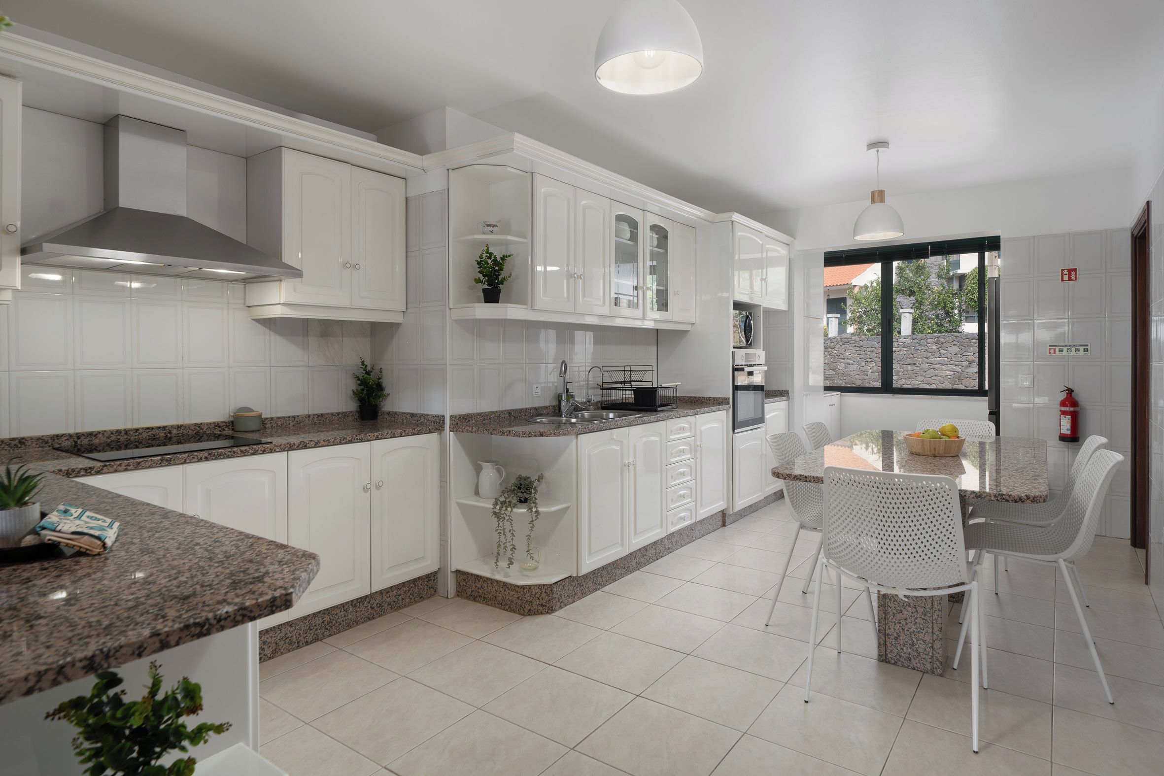 Une cuisine moderne avec des meubles blancs, des plans de travail en granit et un coin repas doté de chaises blanches.