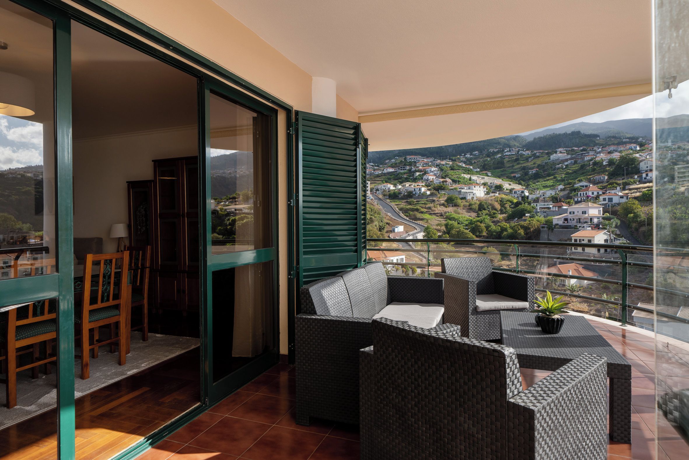 A balcony with wicker furniture and a view of a hillside town.