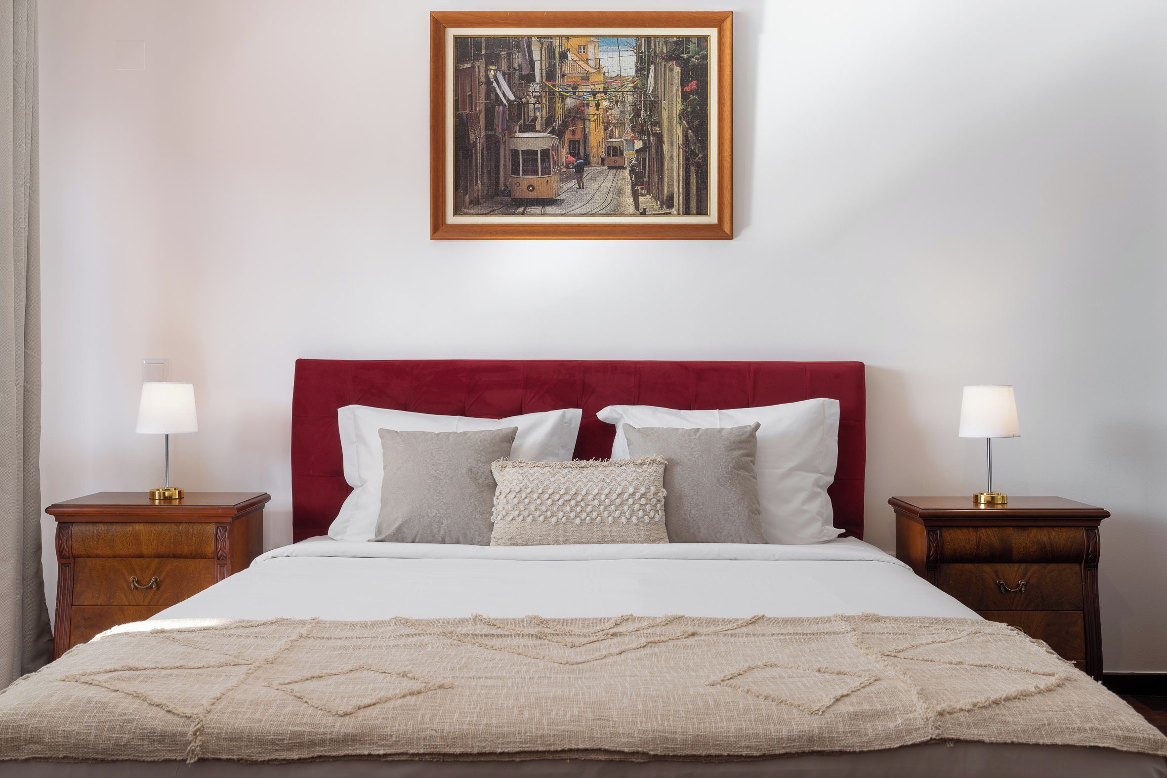 Quarto de hotel com cama grande, duas mesas de cabeceira, cabeceira vermelha e um quadro na parede.