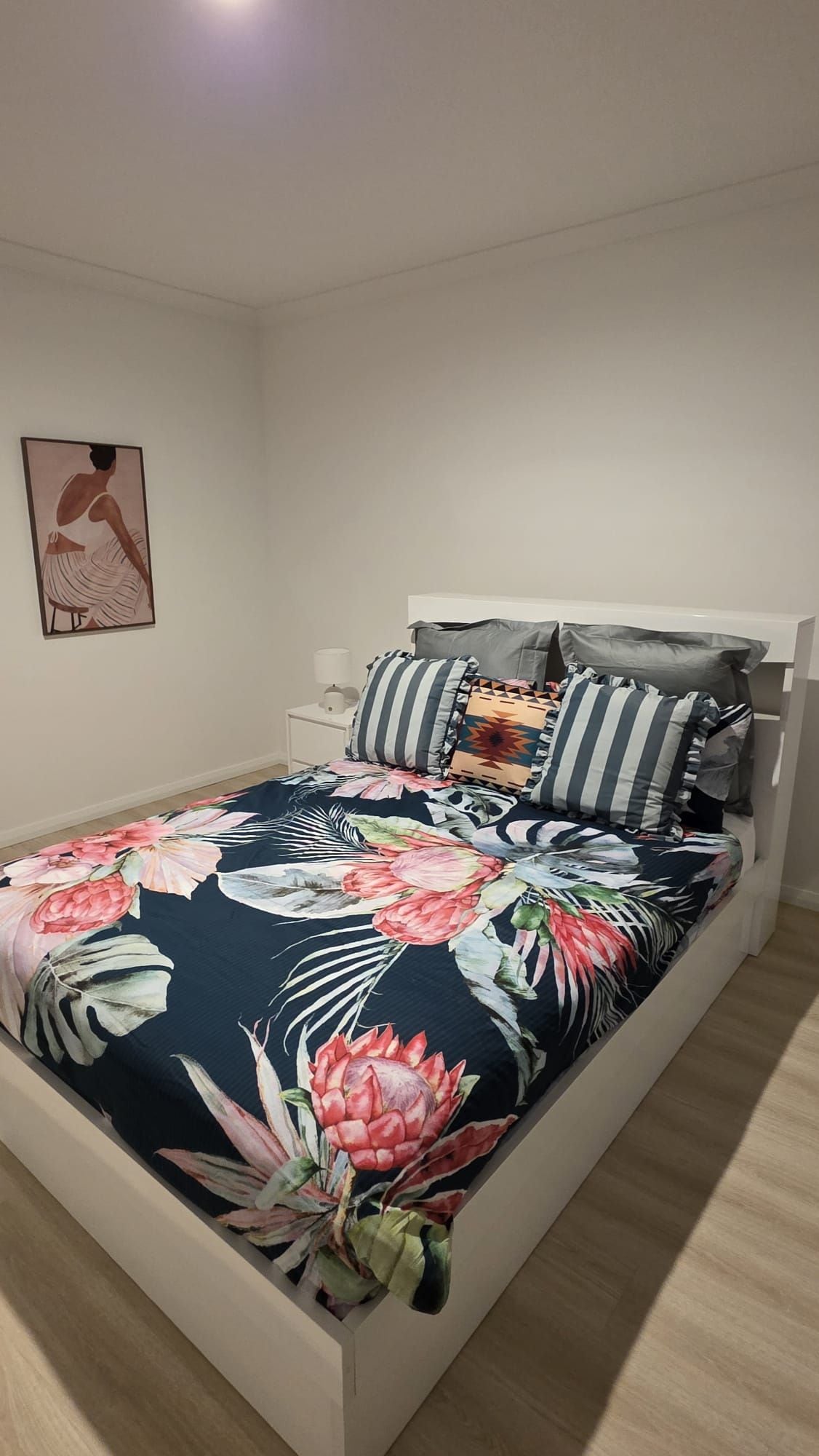A bed with a floral bedspread, a white headboard, and multiple pillows.
