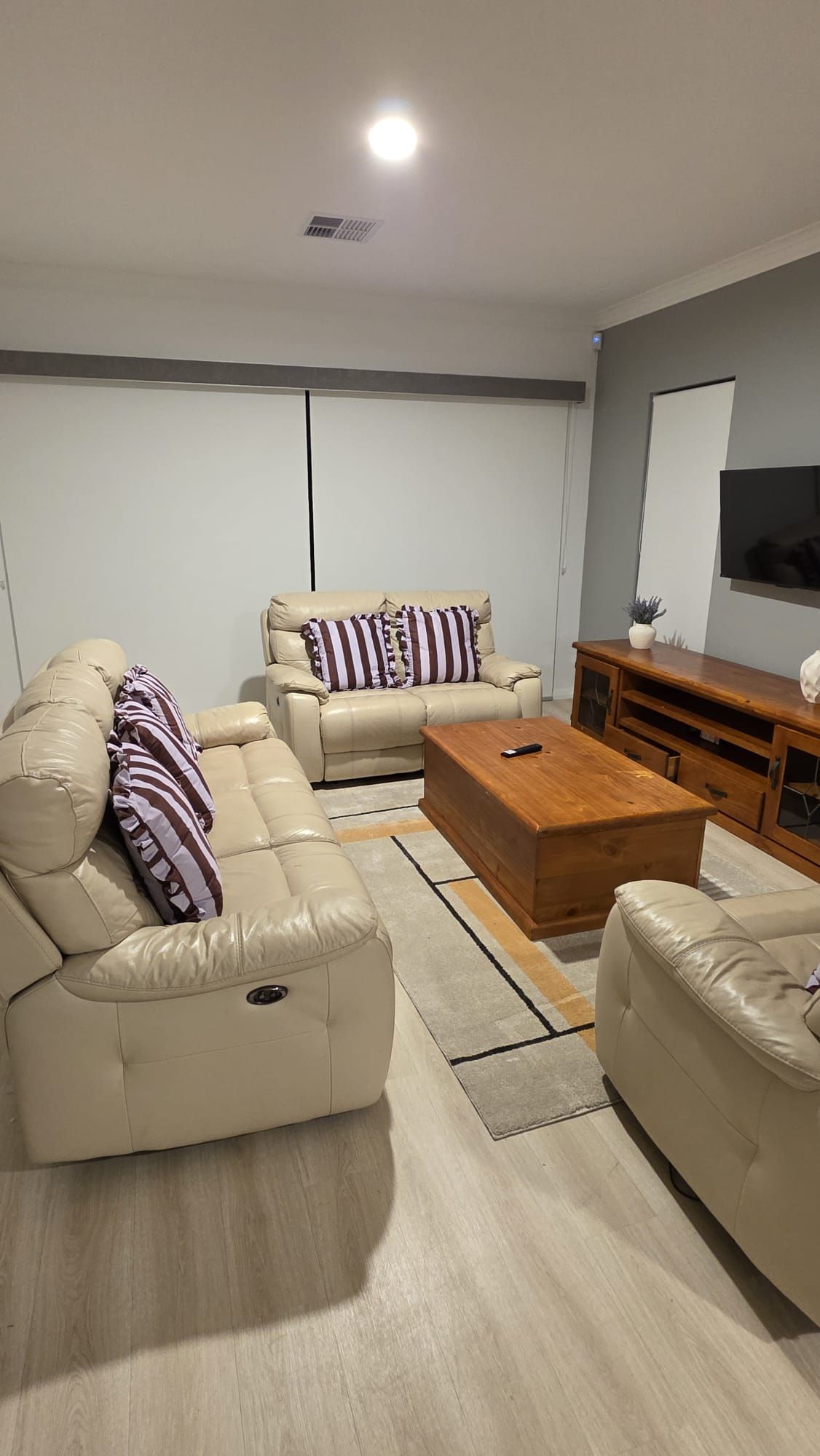 A modern living room with a beige sofa set, a wooden coffee table, and a TV on the wall.