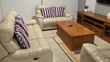 A modern living room with a beige sofa set, a wooden coffee table, and a TV on the wall.
