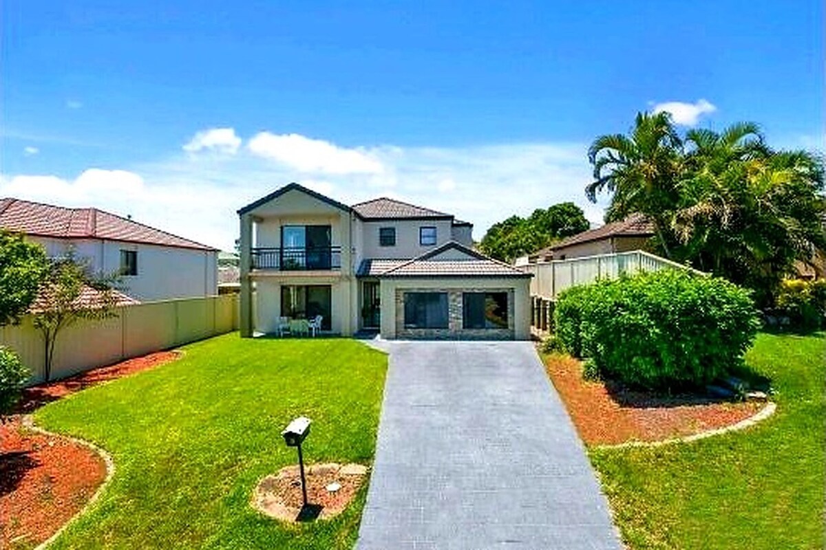 A two-story residential house with a front driveway, a balcony, and a well-maintained lawn.