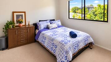 A bedroom with a bed, a nightstand, a dresser, a window with a view, and a ceiling fan.