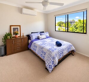 A bedroom with a bed, a nightstand, a dresser, a window with a view, and a ceiling fan. - Room-spacious Master Bedroom (Gold Coast)