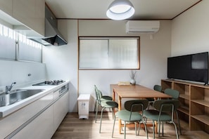 Eine kompakte Küche mit Gasherd, Spüle und eingebautem Backofen. Ein Essbereich mit Holztisch und Stühlen, sowie ein Fernseher auf einem Schrank.