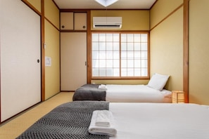 Ein traditionell gestalteter japanischer Raum mit zwei Betten, einem Tatami-Boden, Schiebetüren und einem Fenster mit Gittermuster.