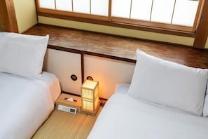Ein Hotelzimmer mit zwei Betten, einem Nachttisch mit Lampe und einem Fenster mit Holzrahmen.
