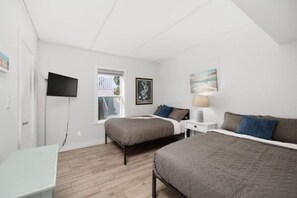Ein Schlafzimmer mit zwei Betten, einem Fernseher, einem Fenster und einem Gemälde.