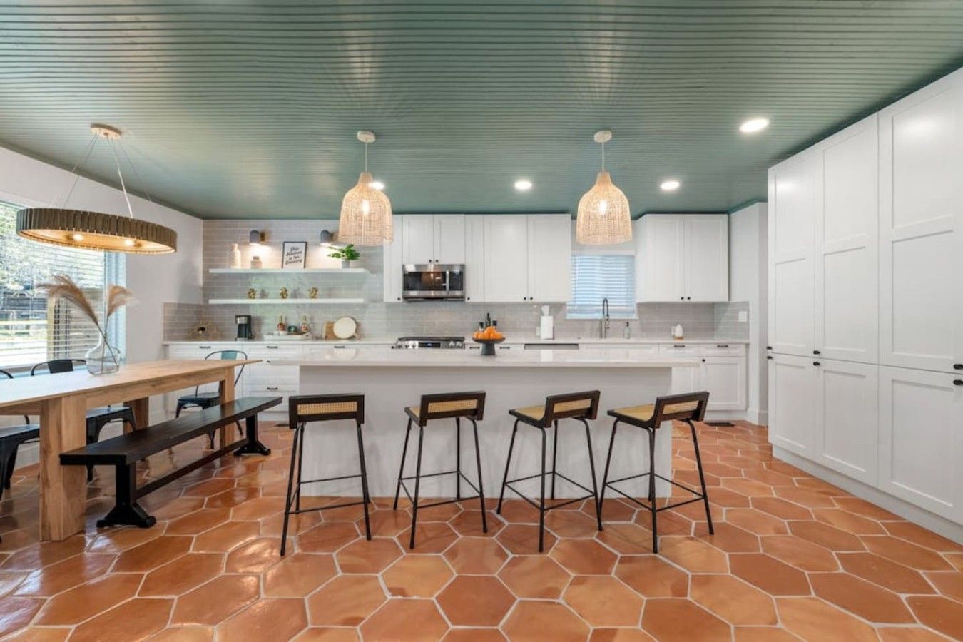 A modern kitchen with white cabinets, a central island with bar stools, and a green ceiling.